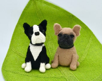 May include: Two crocheted stuffed dogs, a black and white Boston Terrier and a light brown French Bulldog, sitting on a green burlap background.
