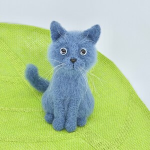 May include: A blue knitted cat toy with white whiskers and large eyes. The cat is sitting on a green knitted leaf.