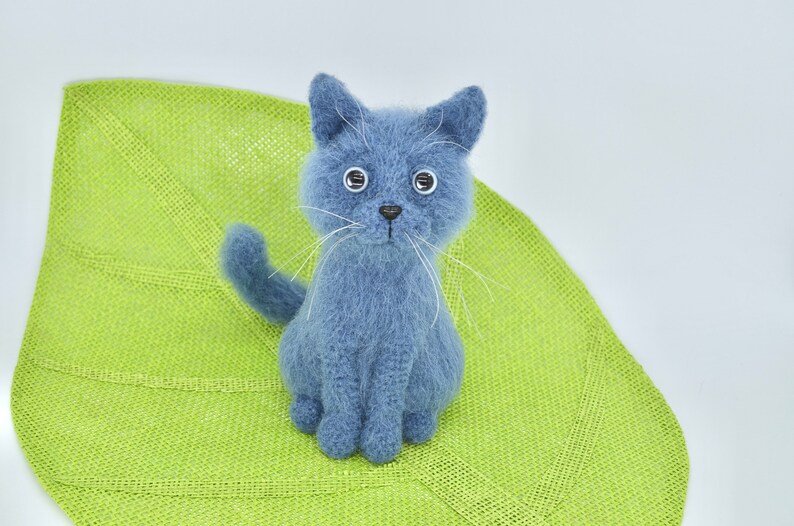 May include: A blue knitted cat toy with white whiskers and large eyes. The cat is sitting on a green knitted leaf.