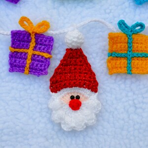May include: A crocheted garland with Santa Claus and gift box ornaments. The garland is white and the ornaments are red, white, purple, yellow, and blue.