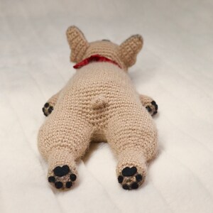 May include: A crocheted stuffed dog toy in a light brown colour with black paw pads and a red bandana around its neck.