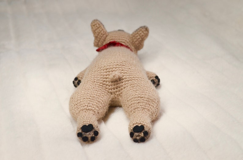 May include: A crocheted stuffed dog toy in a light brown colour with black paw pads and a red bandana around its neck.