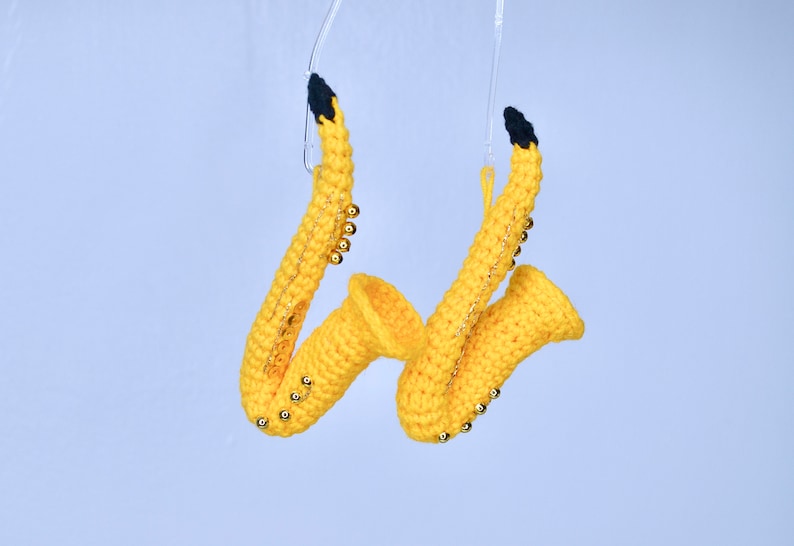 May include: Two yellow crocheted saxophones with gold beads hanging from clear strings.