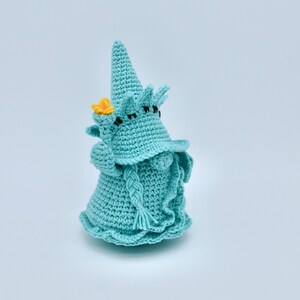 Puede incluir: Un gnomo de crochet con un sombrero puntiagudo, una flor amarilla y una barba trenzada. El gnomo es azul claro y tiene ojos negros.