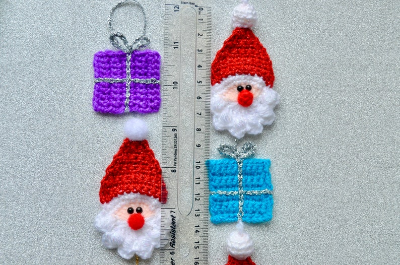 May include: Five crocheted Christmas ornaments, including two Santa Claus figures with red hats and white beards, two gift boxes, one purple and one blue, and one Santa Claus hat.