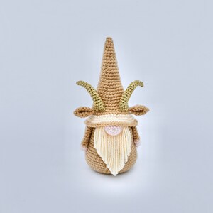 May include: A crocheted gnome with a brown hat and beard, and gold horns. The gnome is standing on a white background.