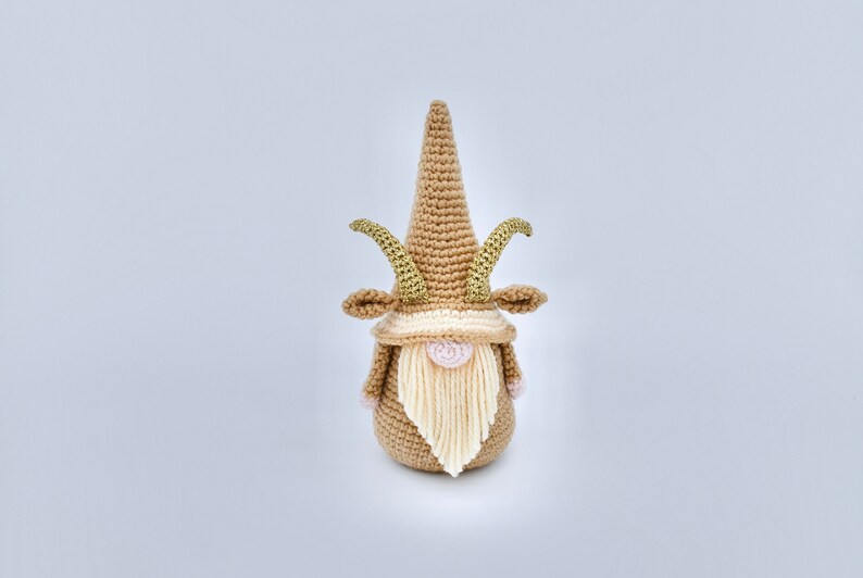 May include: A crocheted gnome with a brown hat and beard, and gold horns. The gnome is standing on a white background.