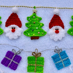May include: A crocheted Christmas garland with green and red Christmas trees, Santa Claus figures, and green and purple gift boxes.