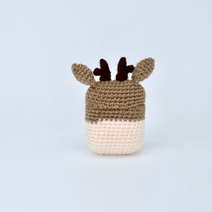 May include: A handmade crochet deer head in shades of brown and cream. The deer has small, dark brown antlers and ears. The crochet work is visible, giving it a textured appearance. The deer head is likely a decorative item or part of a larger craft project.