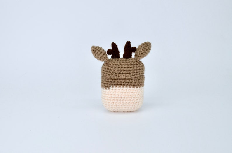 May include: A handmade crochet deer head in shades of brown and cream. The deer has small, dark brown antlers and ears. The crochet work is visible, giving it a textured appearance. The deer head is likely a decorative item or part of a larger craft project.