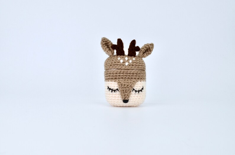 May include: A crocheted deer-shaped container in beige, brown, and cream. The container features closed eyes, a black nose, and small antlers. The deer's face is cream-colored, with a brown top and ears.