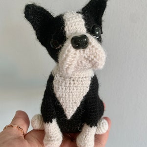 Pu&ograve; includere: Un giocattolo per cani Boston Terrier all'uncinetto, nero e bianco con occhi a bottone neri. Il cane &egrave; seduto con le zampe ripiegate sotto il corpo.