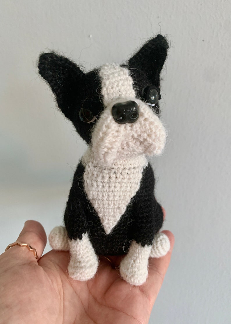 Pu&ograve; includere: Un giocattolo per cani Boston Terrier all'uncinetto, nero e bianco con occhi a bottone neri. Il cane &egrave; seduto con le zampe ripiegate sotto il corpo.