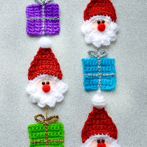 May include: A set of six crocheted Christmas ornaments featuring Santa Claus and presents. The ornaments are red, white, blue, green, and purple. Each ornament has a silver or gold ribbon.