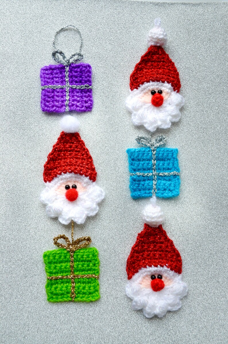 May include: A set of six crocheted Christmas ornaments featuring Santa Claus and presents. The ornaments are red, white, blue, green, and purple. Each ornament has a silver or gold ribbon.