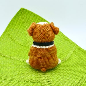 May include: A brown and white crocheted dog toy with a black collar sitting on a green mat.