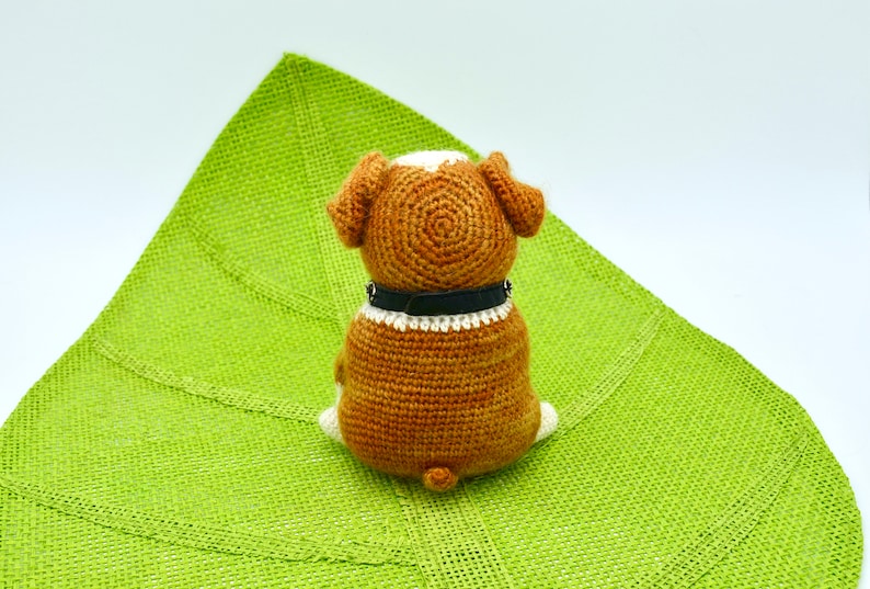 May include: A brown and white crocheted dog toy with a black collar sitting on a green mat.