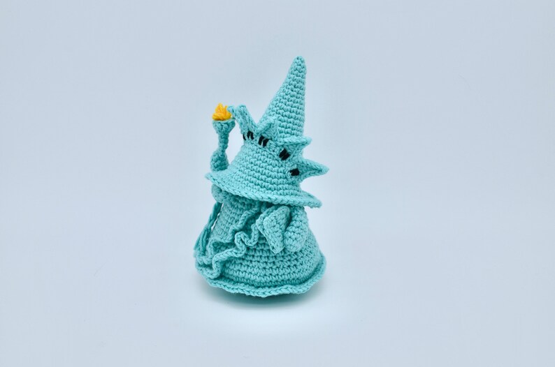 Puede incluir: Una estatua de crochet azul y amarilla de la Estatua de la Libertad. La estatua sostiene una antorcha en su mano derecha.