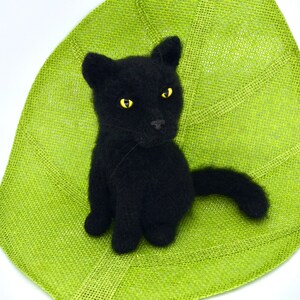 May include: A black knitted cat with yellow eyes sitting on a green burlap leaf.