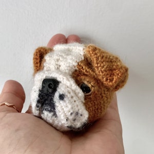 May include: A crocheted bulldog plush toy with brown and white fur. The toy has black eyes and a black nose.