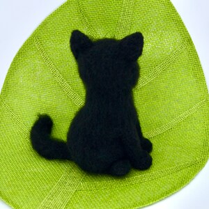 May include: Black knitted cat figurine sitting on a green burlap surface.