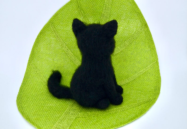 May include: Black knitted cat figurine sitting on a green burlap surface.