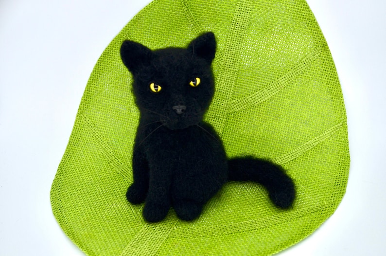 May include: A black cat plush toy with yellow eyes, sitting on a green leaf-shaped mat.