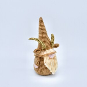 May include: A crocheted gnome with a brown hat and a long white beard. The gnome has gold antlers and a pink nose.