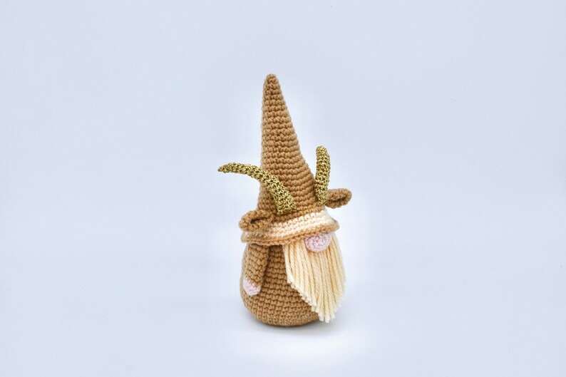May include: A crocheted gnome with a brown hat and a long white beard. The gnome has gold antlers and a pink nose.