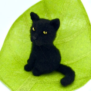 May include: A black crocheted cat with yellow eyes sitting on a green textured surface.