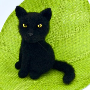 May include: A black knitted cat figurine with yellow eyes sitting on a green burlap surface.