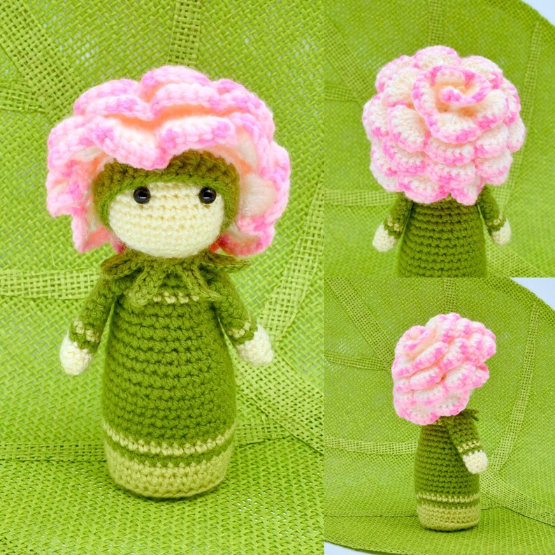 Op de afbeelding: Een gehaakte pop met een roze en witte bloemenhoed en een groene jurk. De pop staat op een groen geweven oppervlak.
