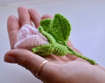 Peut inclure: Une rose rose en crochet avec des feuilles vertes. La rose est tenue dans une main avec une bague en or.