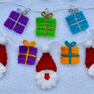 May include: A crocheted Christmas garland with alternating red Santa figures and colorful gift boxes. The garland is strung with silver thread and features a variety of colors, including red, green, blue, purple, and yellow.