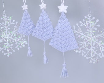 Op de afbeelding: Drie gehaakte lichtblauwe kerstboomversieringen met witte sterretjes en witte kwastjes die aan een witte achtergrond hangen.