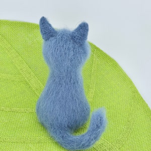 May include: A blue knitted cat toy sitting on a green leaf-shaped mat.