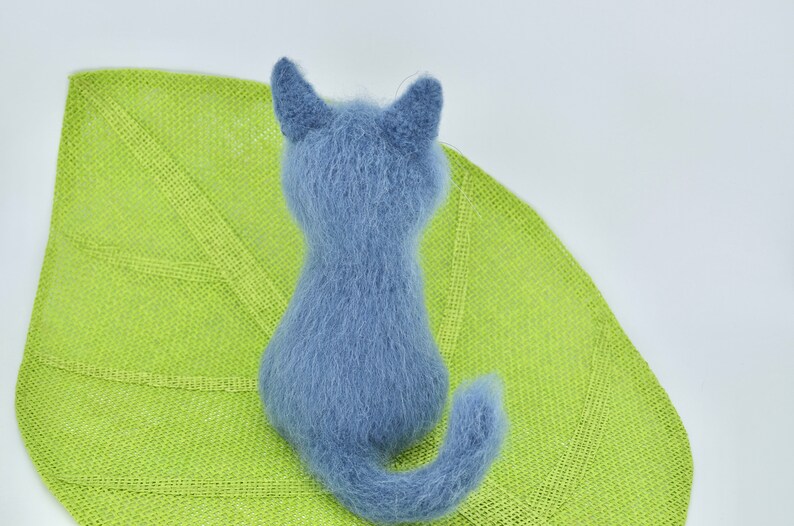 May include: A blue knitted cat toy sitting on a green leaf-shaped mat.