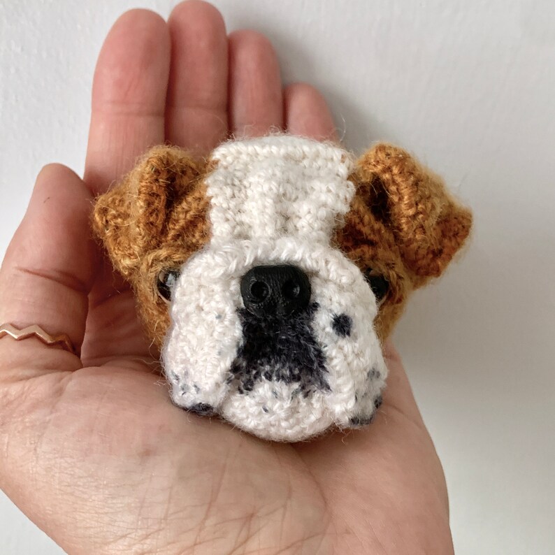 May include: A crocheted bulldog amigurumi toy with brown ears, a white face, and black nose and eyes.