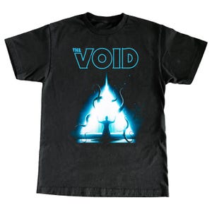 May include: Black t-shirt featuring the text "THE VOID" in light blue. The graphic depicts a glowing blue triangle with a silhouetted figure and swirling tentacles. The design has a cosmic or sci-fi theme.