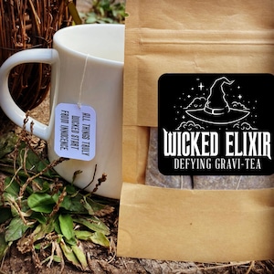 Könnte beinhalten: Ein brauner Papierbeutel mit einem schwarz-weißen Logo, auf dem "Wicked Elixir Defying Gravi-Tea" steht. Das Logo zeigt einen Hexenhut mit Sternen. Ein weißer Teebeutel mit dem Text "All things truly wicked start from innocence" befindet sich vor dem Beutel.