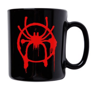 Puede incluir: Taza de cer&aacute;mica negra con un s&iacute;mbolo de Spider-Man rojo. El s&iacute;mbolo es un c&iacute;rculo rojo con una ara&ntilde;a dentro, y el c&iacute;rculo tiene gotas de pintura roja que salen de &eacute;l.