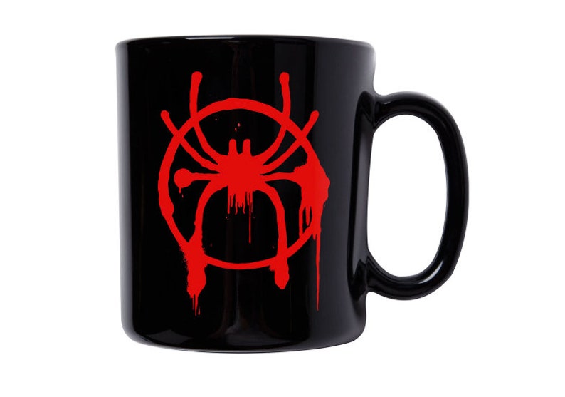 Puede incluir: Taza de cer&aacute;mica negra con un s&iacute;mbolo de Spider-Man rojo. El s&iacute;mbolo es un c&iacute;rculo rojo con una ara&ntilde;a dentro, y el c&iacute;rculo tiene gotas de pintura roja que salen de &eacute;l.