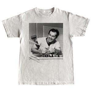 Puede incluir: Camiseta blanca con una imagen en blanco y negro de un hombre riendo. La imagen muestra al hombre en un entorno médico, sosteniendo una herramienta. La camiseta está hecha de un material suave y cómodo.