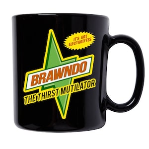Op de afbeelding: Zwarte keramische mok met een groene en gele stervormige afbeelding. De ster heeft de tekst "BRAWNDO" en "THE THIRST MUTILATOR" erop. Een gele cirkel met de tekst "IT'S GOT ELECTROLYTES" bevindt zich boven de ster.