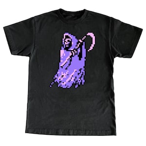 Puede incluir: Camiseta negra con una imagen pixelada de la Muerte en morado y rosa.
