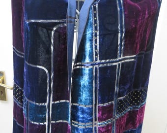 May include: A velvet scarf featuring a geometric patchwork design in shades of deep purple, royal blue, and turquoise. The fabric is accented with thin silver lines and small gold dot patterns, finished with black fringe at the bottom edges.