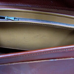 May include: A brown leather bag with a zippered pocket. The pocket is lined with a light brown fabric.