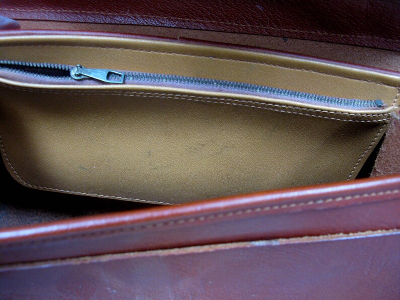 May include: A brown leather bag with a zippered pocket. The pocket is lined with a light brown fabric.