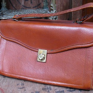 May include: A brown leather satchel with a brass clasp. The bag has a flap closure and a top handle.