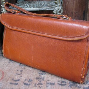 May include: A brown leather handbag with a flap closure and a short handle. The bag has a worn, vintage look.